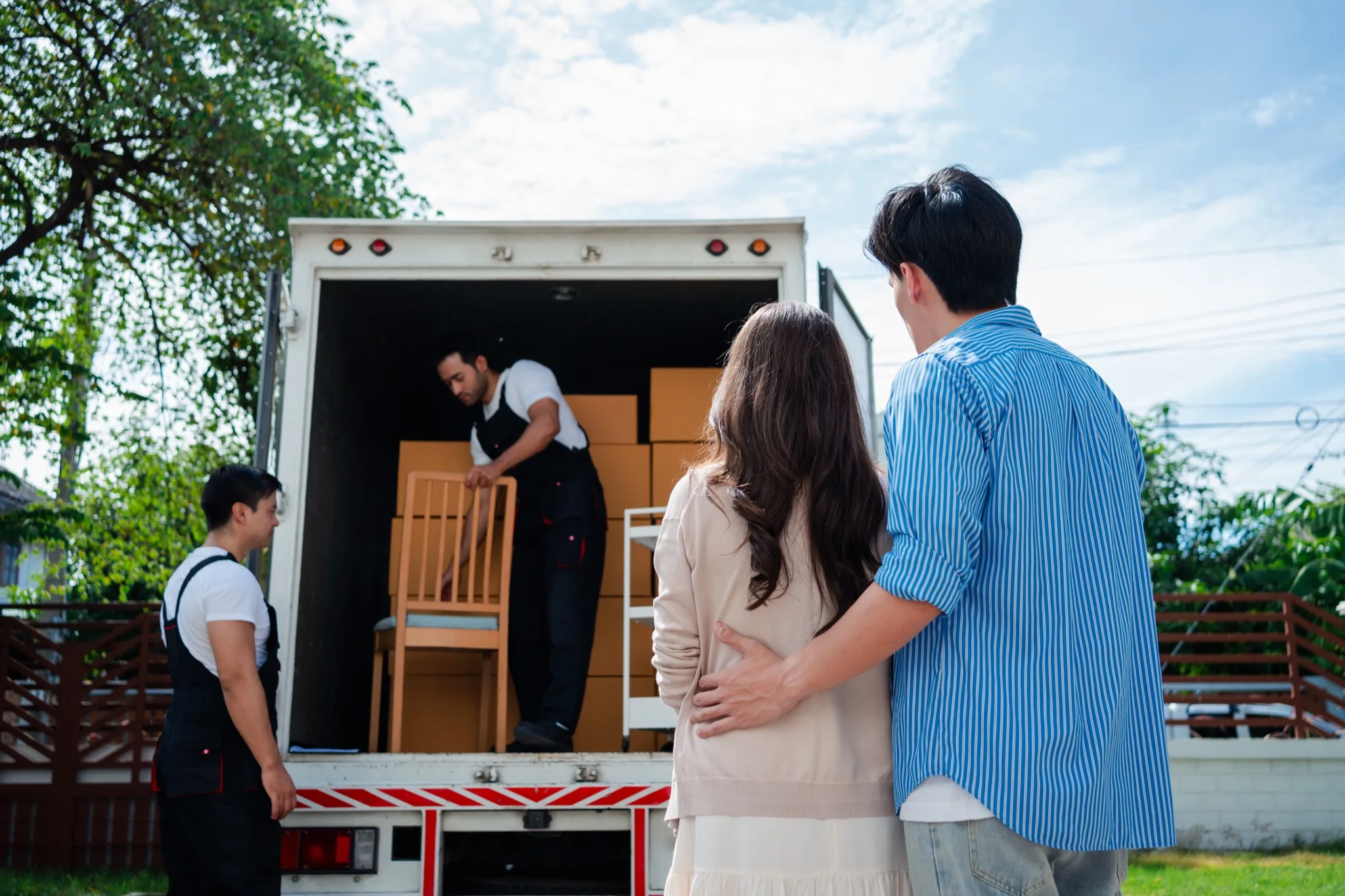 Moving crew loading a truck while a couple watches at their new home