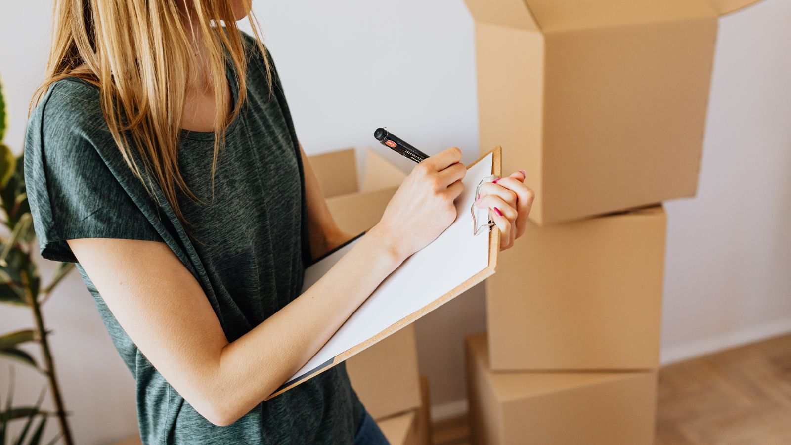 Person writing on a moving checklist beside packed boxes
